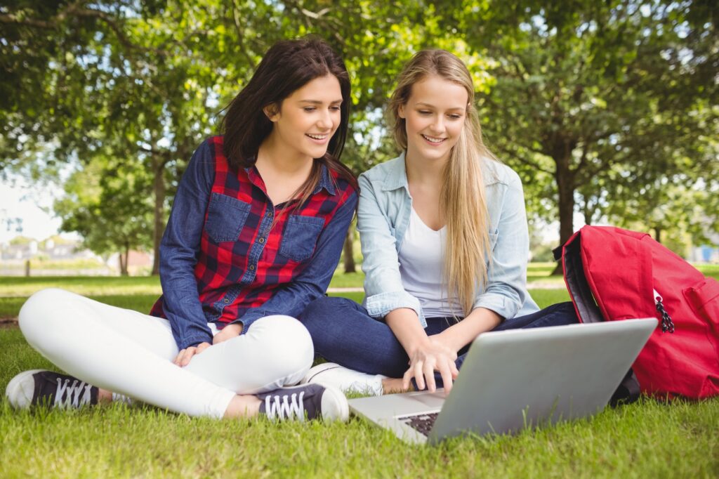 Female students using a laptop while sitting in the school's green space